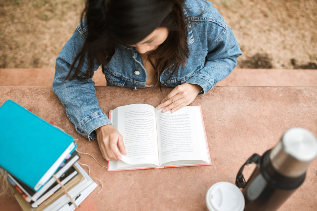 A person reading a horror book with coffee and a stash of books