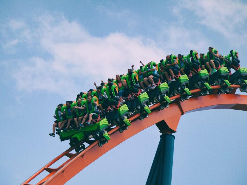 A group of people riding a green and orange roller coaster. 