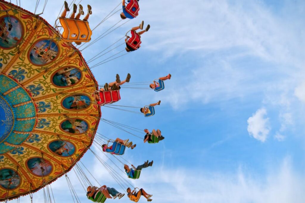 A group of young adults riding a colorful carnival swing ride against a blue sky.